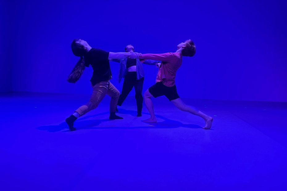 3 dancers locking arms in a circular shape against a bright blue background