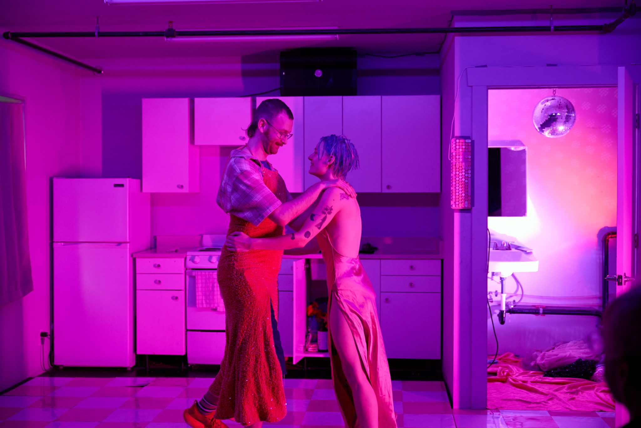 kelly dancing with shane wearing a red dress in the kitchen with pink lighting