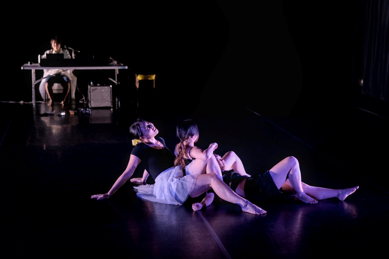 Two dancers in MayDay MayDay MayDay on the floor against a dark background