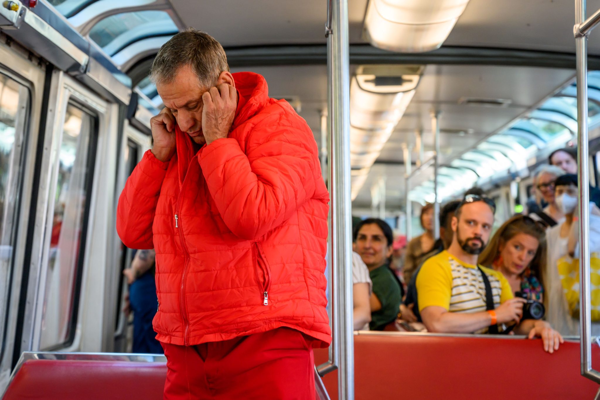 Haim wearing red lowering head and covering ears on the monorail