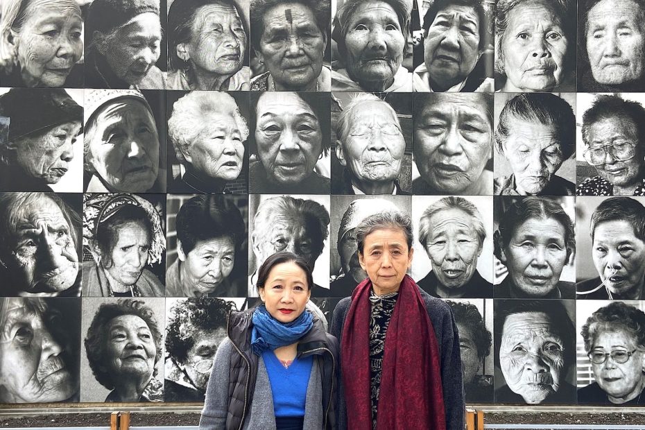 Wen Hui and Eiko in Nanjing in front of a wall of black and white photos